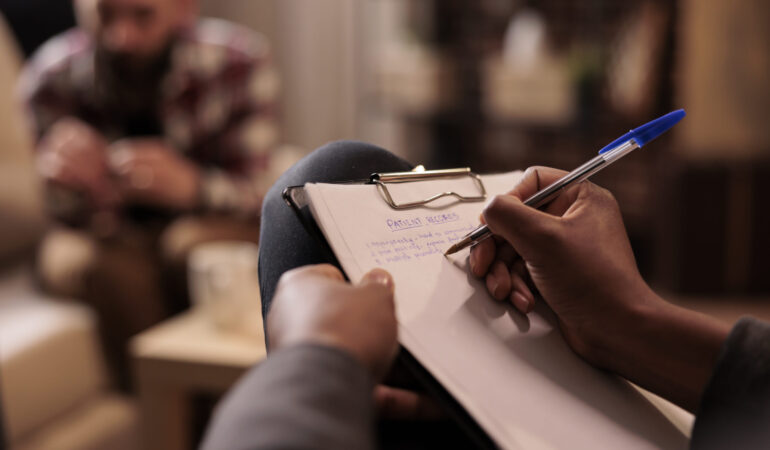 Male psychologist taking notes at couple therapy session to help with relationship issues, counselor giving advice. Explaining marriage problems, using paper to do psychoanalysis. Close up,